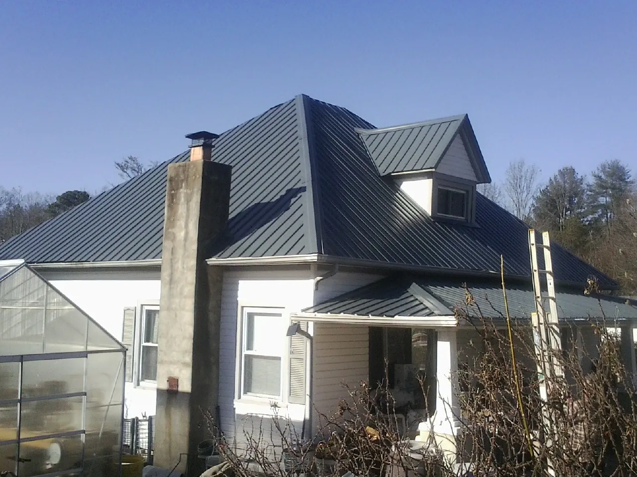 Dark blue standing seam metal roof on a white farmhouse with dormer — Slate & Tile Roof Repair by Roofing Brothers in Hazelwood