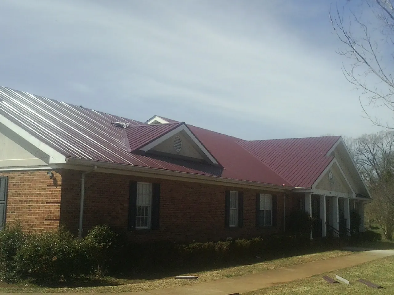 Red metal roof with gabled entries on a long brick building, from a Hail Damage Roof Repair job in Hazelwood