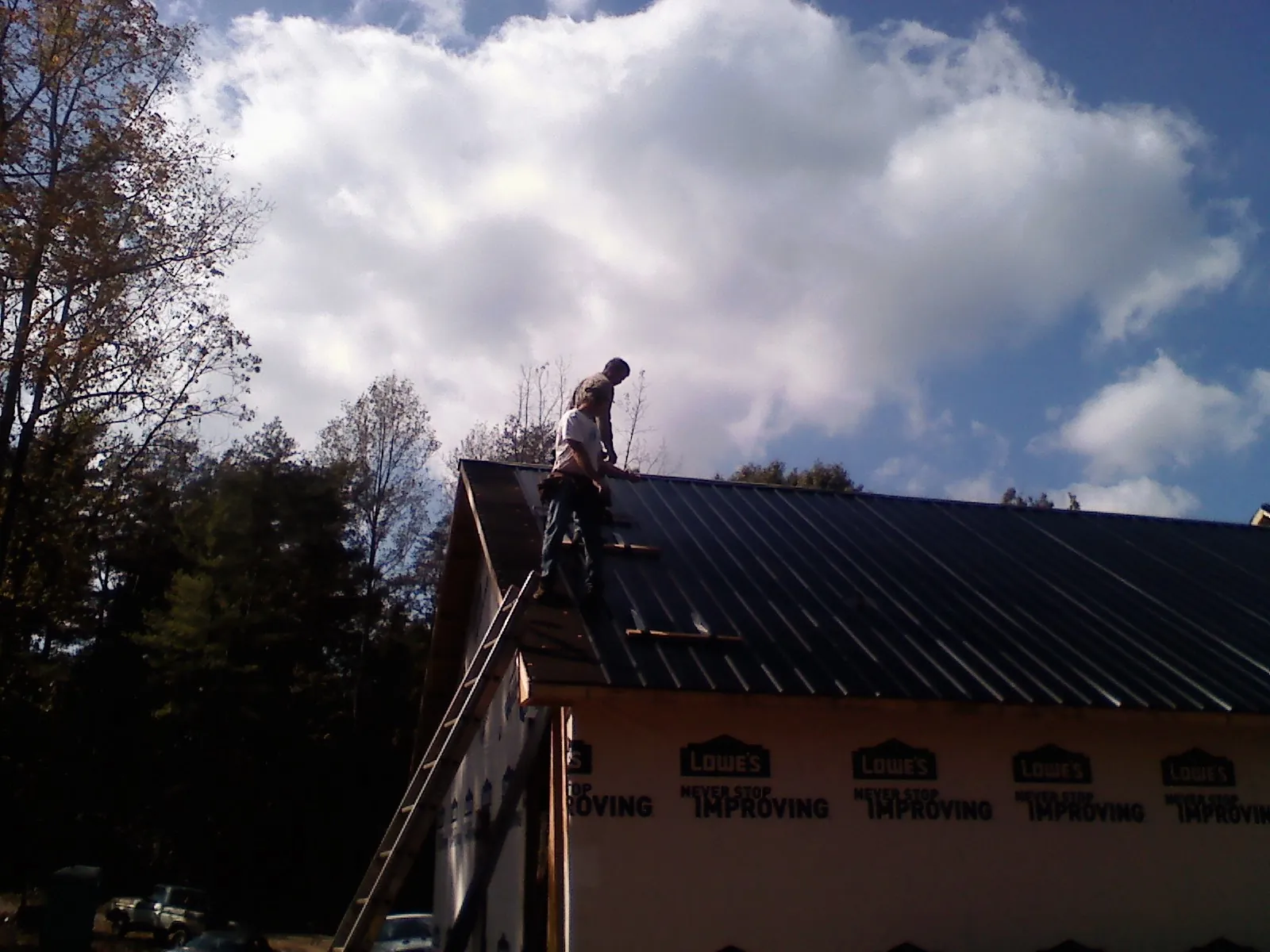 Roofer fastening dark metal panels high against a cloudy sky, from a Roof Inspection job in Hazelwood