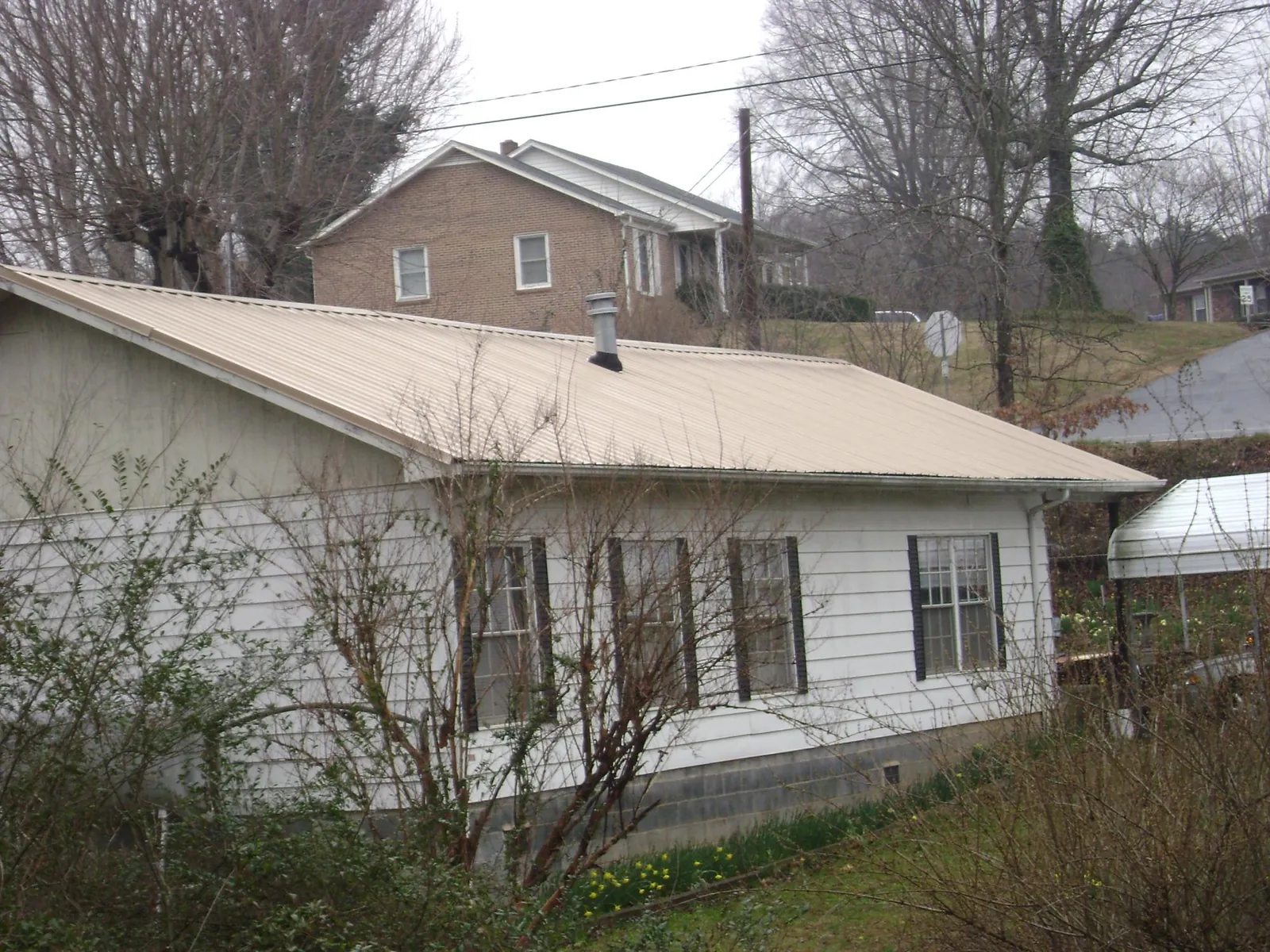 Tan metal roof on a white sided house set into a hillside — Commercial Roofing by Roofing Brothers in Hazelwood
